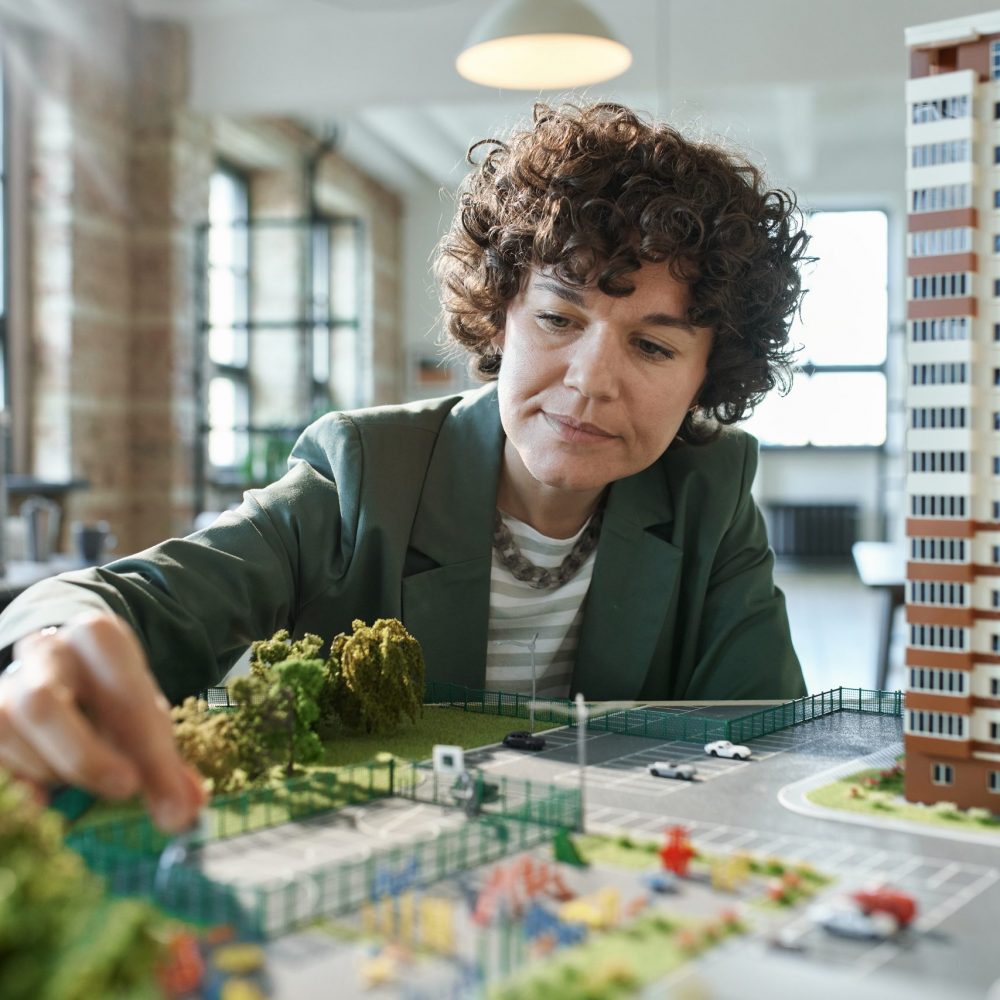 Young female architect working over mock-up of building, she developing new construction project at office